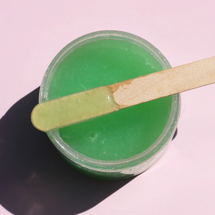Lycon Apple & Cranberry Sugar Scrub 520g in een pot met groene suikerbodyscrub en een houten spatula.