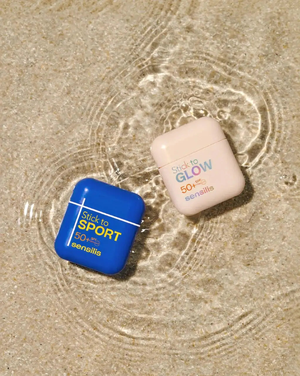 Sensilis Stick to Glow SPF50+ 10gr. en Stick to Sport SPF50+ naast elkaar in water, met stralende uitstraling en effectieve zonbescherming.