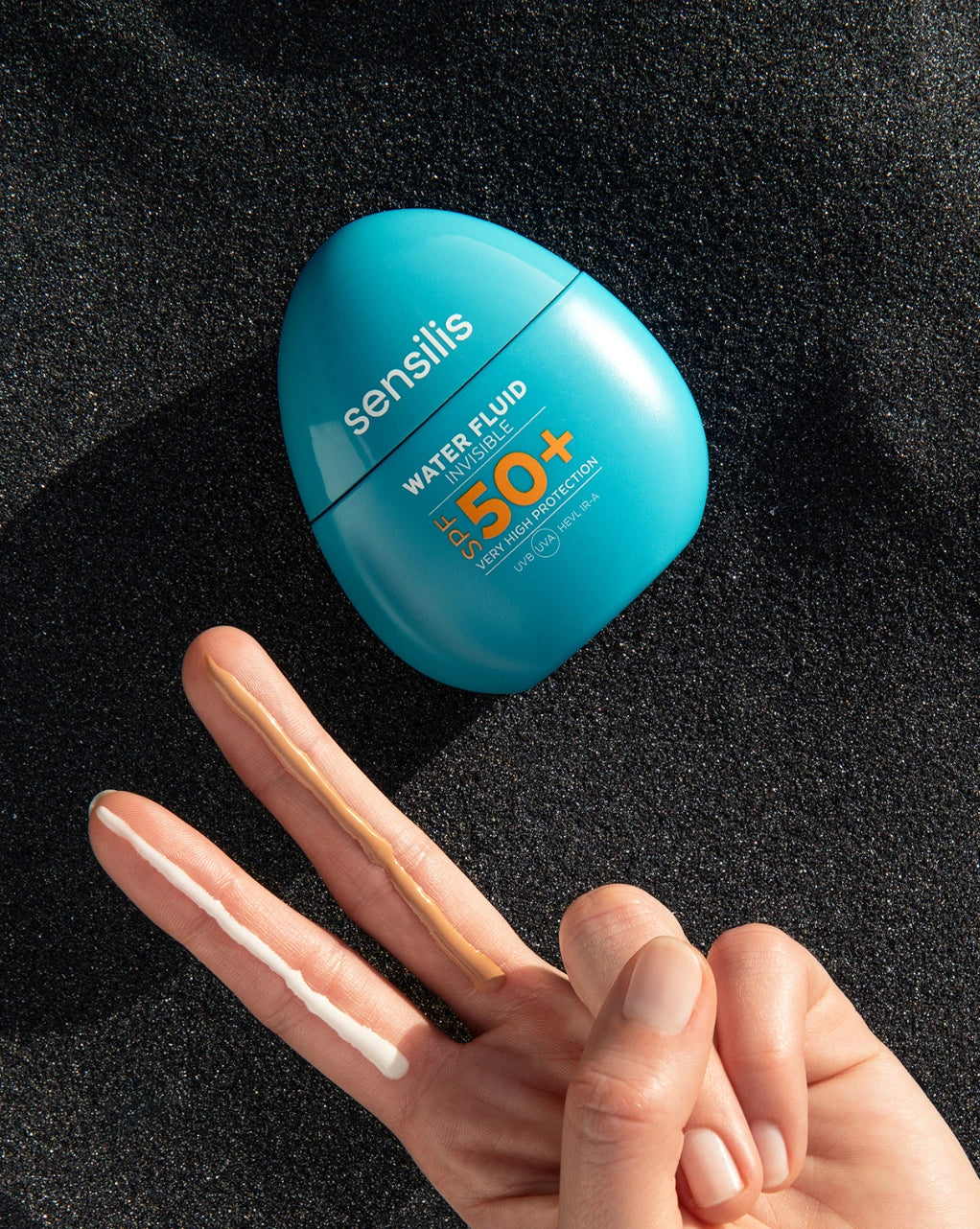 Sensilis Water Fluid 50+ 40ml met een hand en zonnecrème strepen op een zandachtige ondergrond